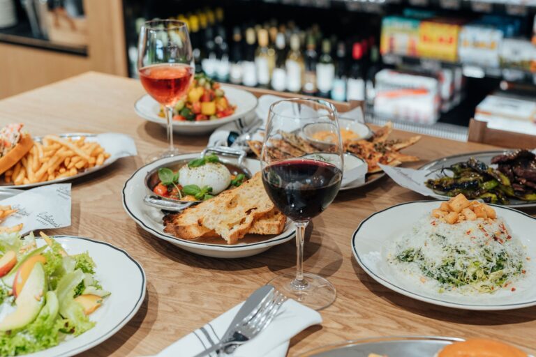 Gourmet dining spread at Littleton’s Market featuring fresh salads, burrata with toasted bread, steak, vegetables, and glasses of wine.
