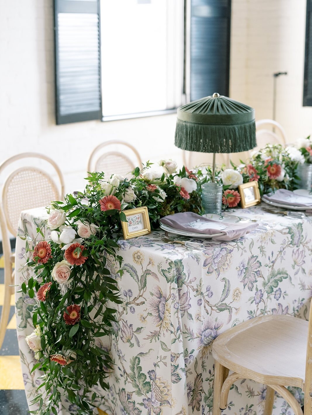 Romantic Columbus wedding reception tablescape featuring cascading pink and white florals by Market Blooms, patterned linens, green fringed lamps, and gold-framed place cards.