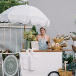 Market Blooms floral cart featuring fresh hydrangeas, wrapped bouquets, and a white fringed umbrella at an outdoor Columbus event.