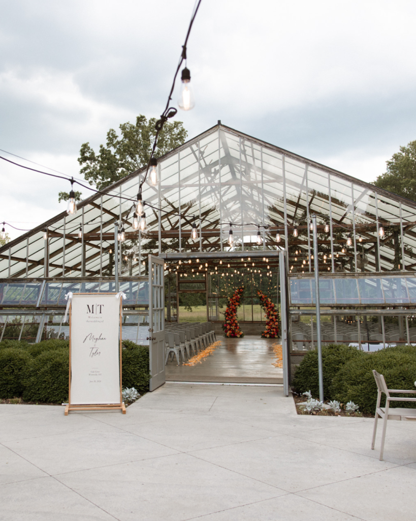 Glass greenhouse wedding ceremony venue at Jorgensen Farms Oak Grove in Westerville, Ohio, decorated with string lights and vibrant floral arrangements.