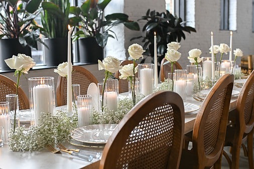 Elegant Columbus Ohio wedding reception with wooden cane-back chairs, white roses, baby's breath floral arrangements, glowing pillar candles, and taper candles arranged along a beautifully styled banquet table.