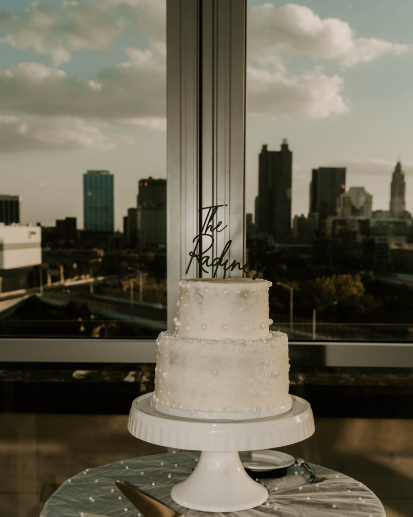Elegant two tier white wedding cake decorated with pearl details and a personalized cake topper, displayed against the downtown Columbus Ohio skyline.