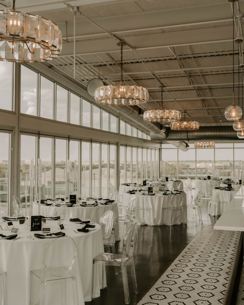 Elegant black and white wedding reception at North 4th Corridor in Columbus Ohio featuring clear ghost chairs, white table linens, black napkins, and crystal chandeliers.