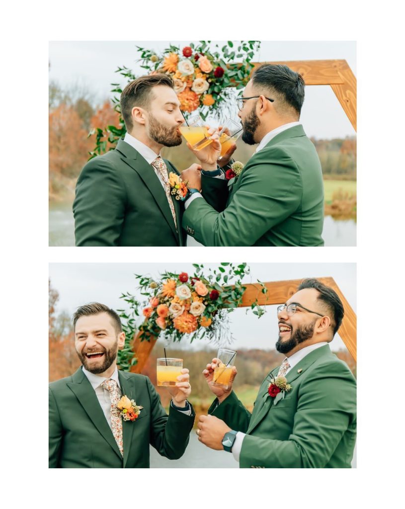 Grooms in green suits stand in front of a wooden ceremony arbor adorned with florals while sipping from drinks and laughing