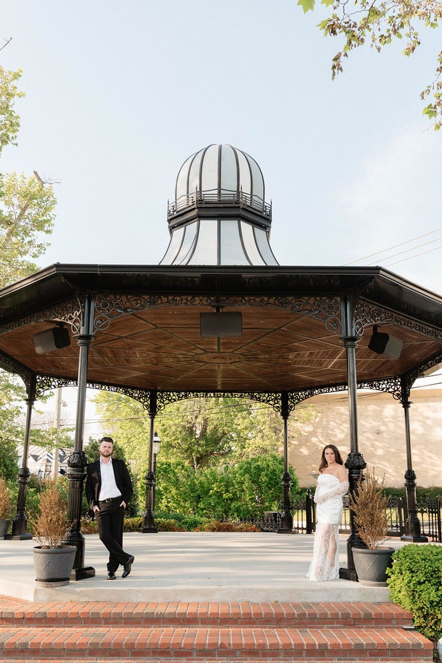 man and women stand under canopy dressed in a suit and white dress