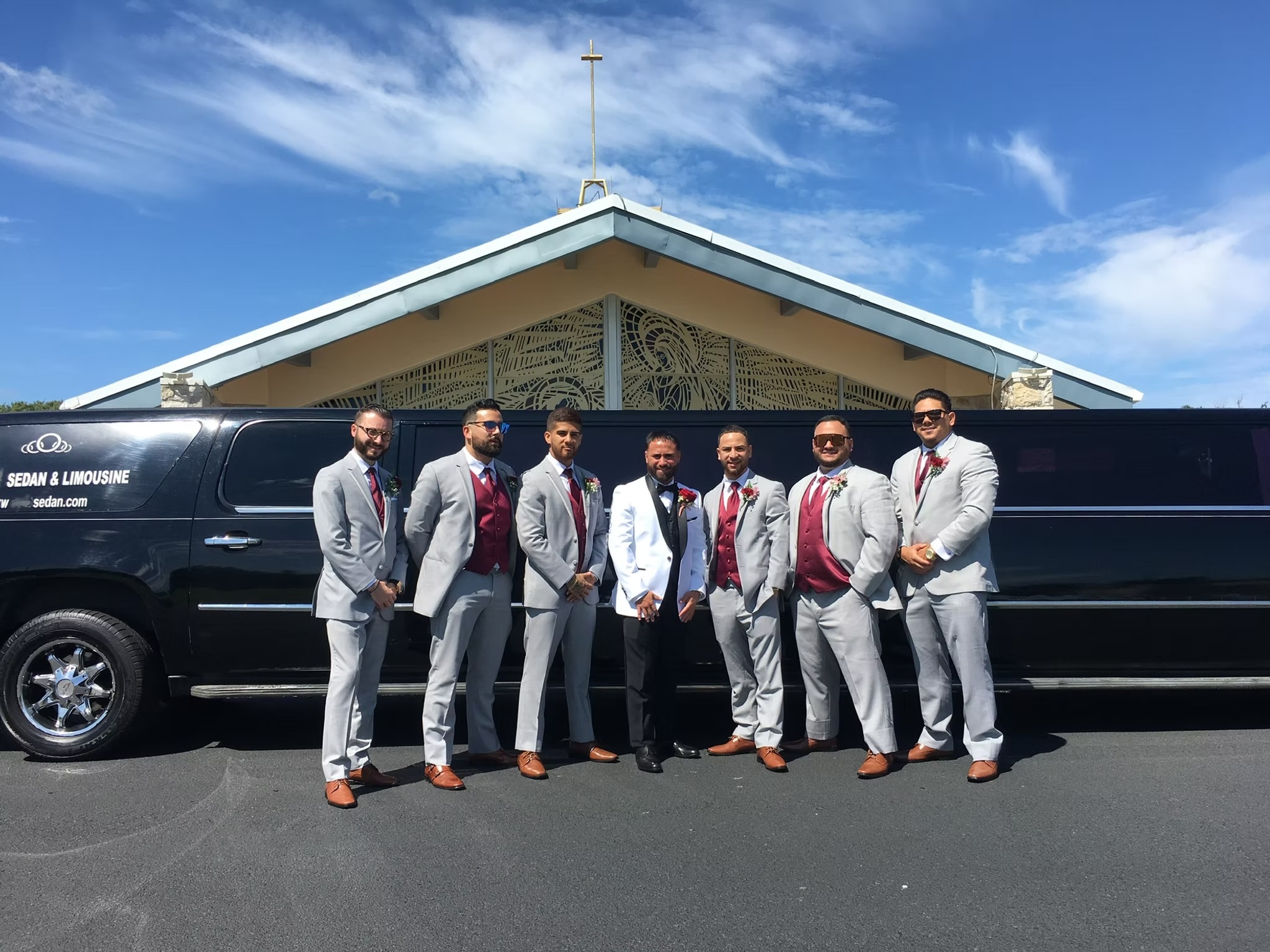 Smiling bride in a lace gown and veil sits with four bridesmaids in shimmering champagne-gold gowns inside a wedding party bus. They all stretch out their hands to show off their rings and manicures, a fun getaway moment for South Jersey weddings and bridal party transportation.
