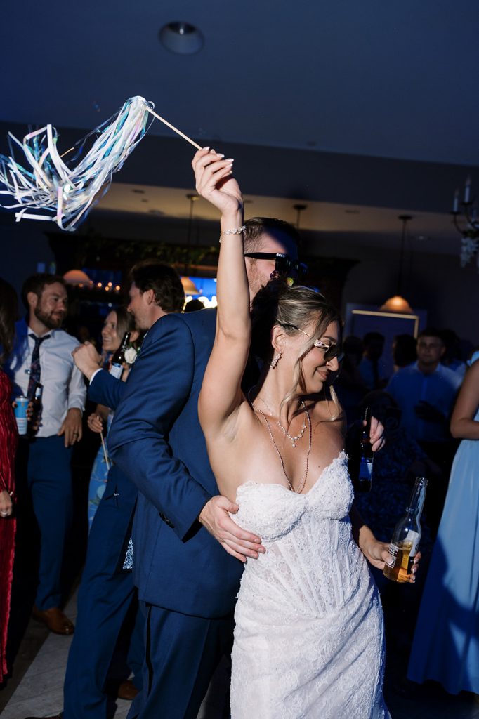 Bride and groom dancing on a crowded dance floor during the reception, with the bride holding a ribbon wand in the air.