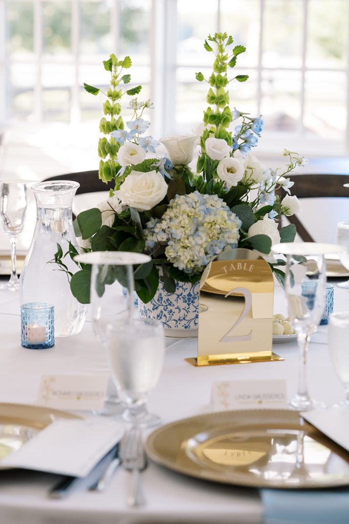 Elegant wedding reception tablescape featuring a white and blue floral centerpiece, gold-rimmed glassware, and place settings.